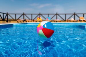 A bright inflatable multicolored ball floats on the surface of clean transparent water in a blue clear pool under the warm summer sun. Pools represent an area where slip and falls happen from wet conditions.