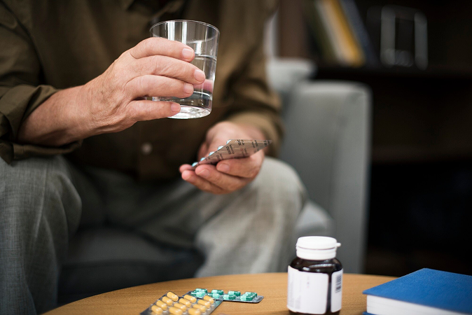 An elderly man with a glass of water and some medications or vitamins.