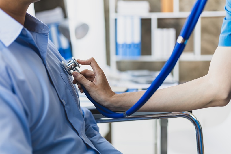 Female doctor using stethoscope examining patient in wheelchair for diagnosis in hospital examination room.