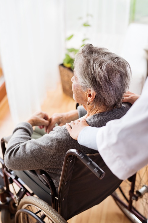 An elderly woman is sitting in a chair while a caregiver massages her shoulders.