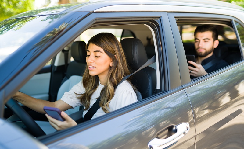 A woman is driving, distracted on her phone.
