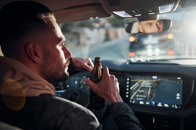 A man is driving a car while drinking alcohol.