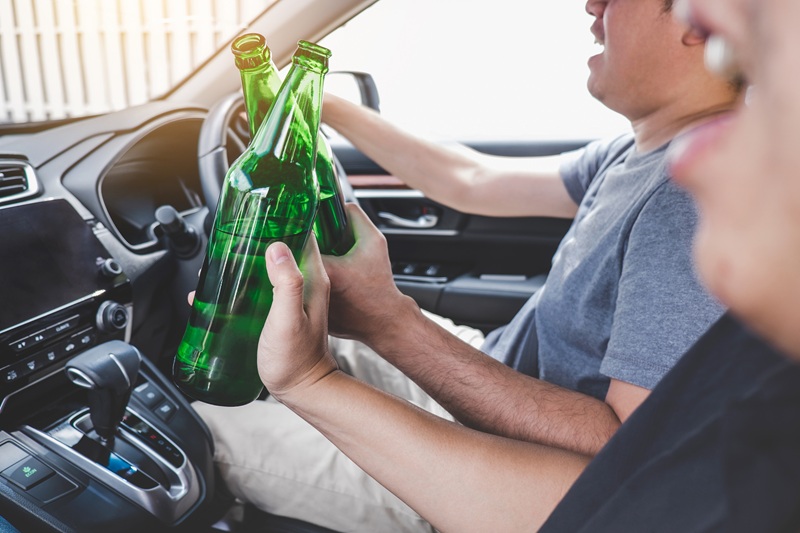 A driver and a passenger are drinking what appears to be alcohol while operating a motor vehicle.