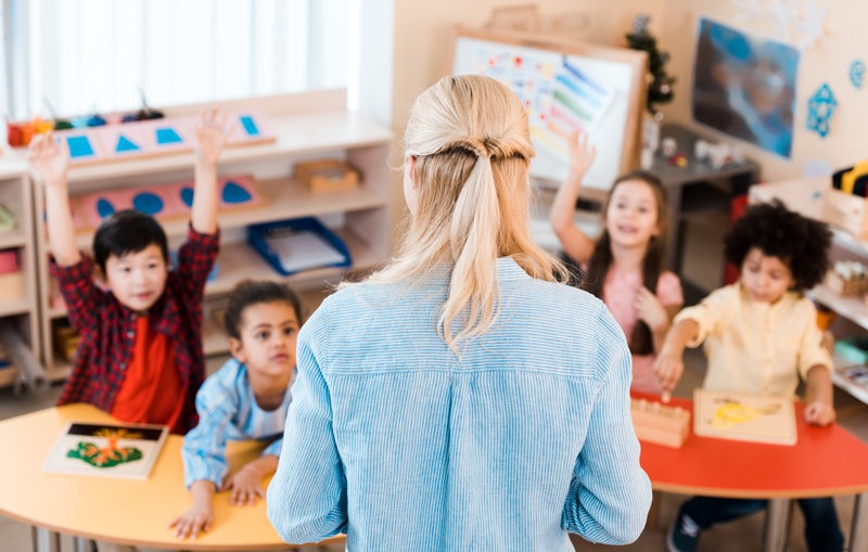 A daycare teacher is standing in front of children teaching them.