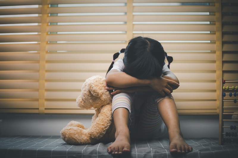 Close up lonely little girl hugging toy, sitting at home alone, upset unhappy child waiting for parents, thinking about problems, bad relationship in family, psychological trauma