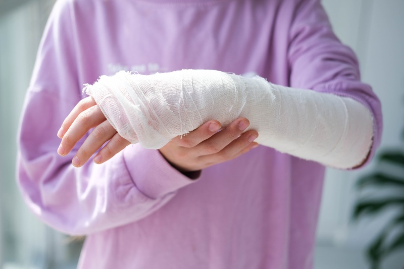 Close up image of a woman in a pink sweater. She has a cast on her arm from an injury.