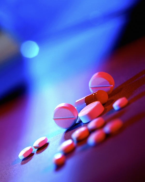 A closeup image of different pills on a table in bright blue and pink light.
