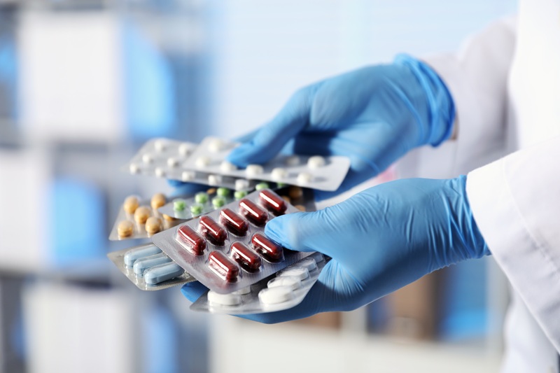 Pharmacist holding blisters with different pills in clinic, closeup
